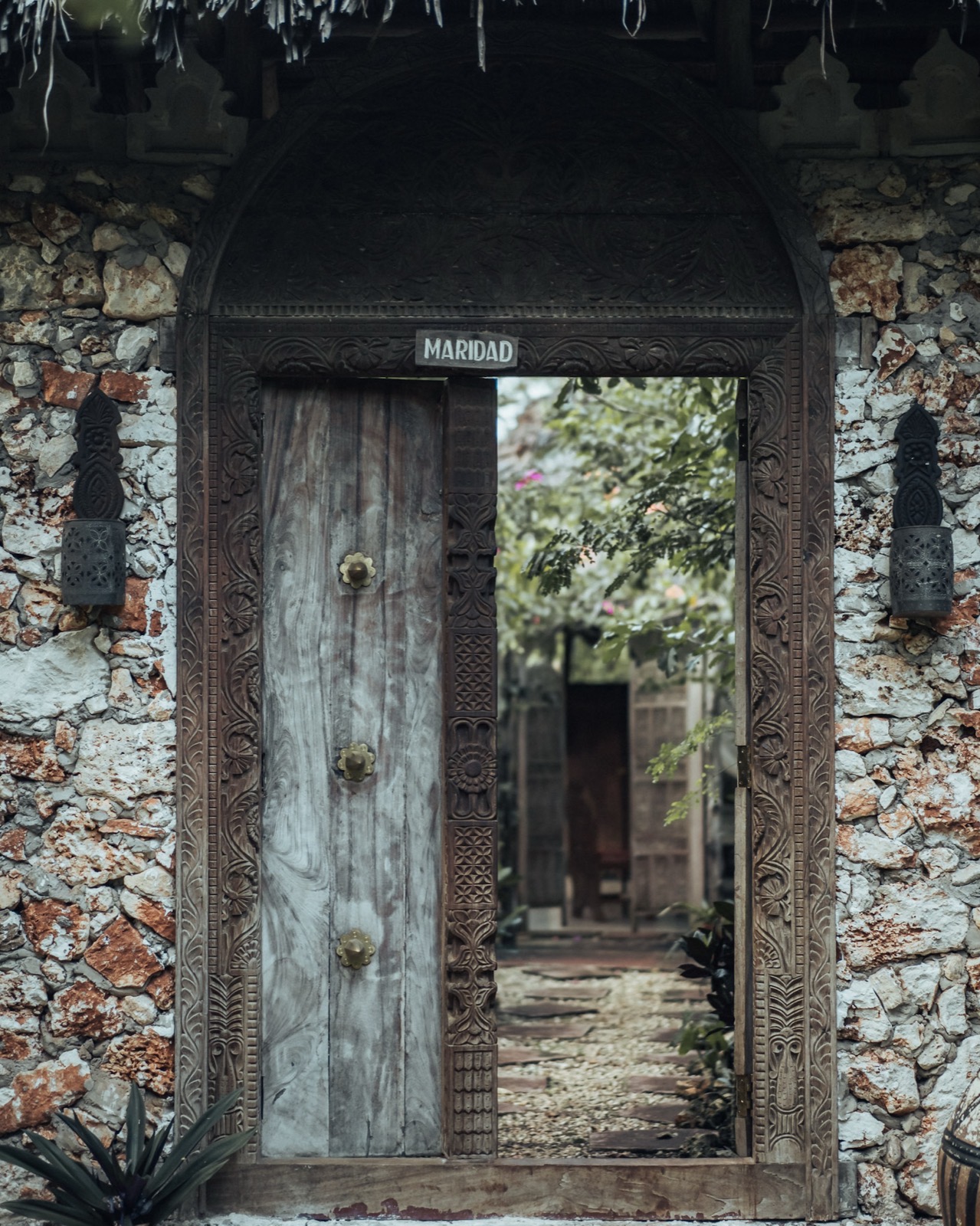 Ornate carved wooden doorway with stone wall and tropical foliage in a Zanzibar coastal village