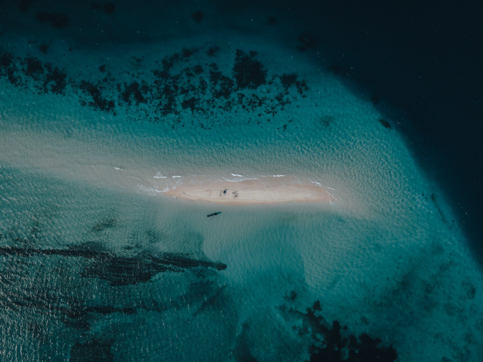 Aerial view of Mnemba Atoll — a narrow sandbar surrounded by deep turquoise Indian Ocean water and coral reef