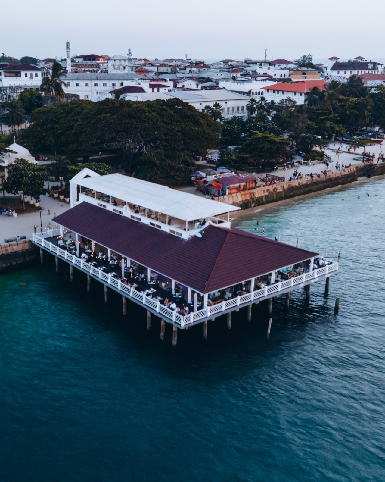 Restaurant and bar on a pier over the Indian Ocean with Stone Town visible in the background at dusk